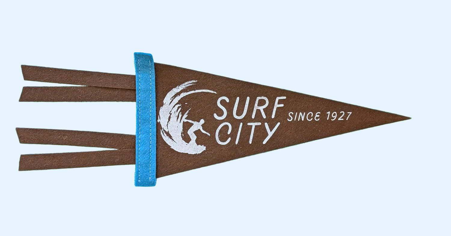 Surf City, Since 1927 souvenir pennant representing Santa Cruz California with a surfer in a wave on brown felt