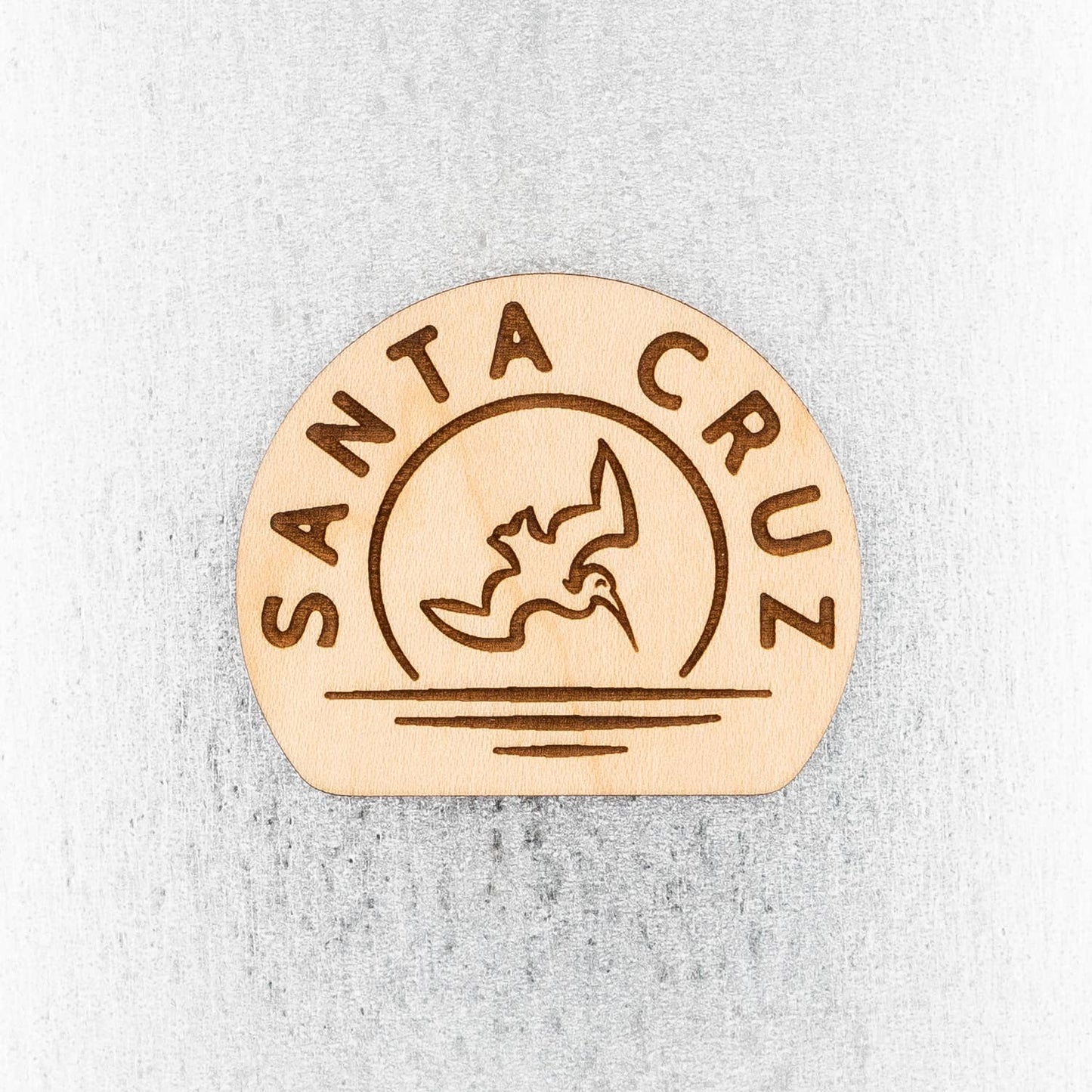Wooden magnet with Santa Cruz and pelican diving into ocean at sunset