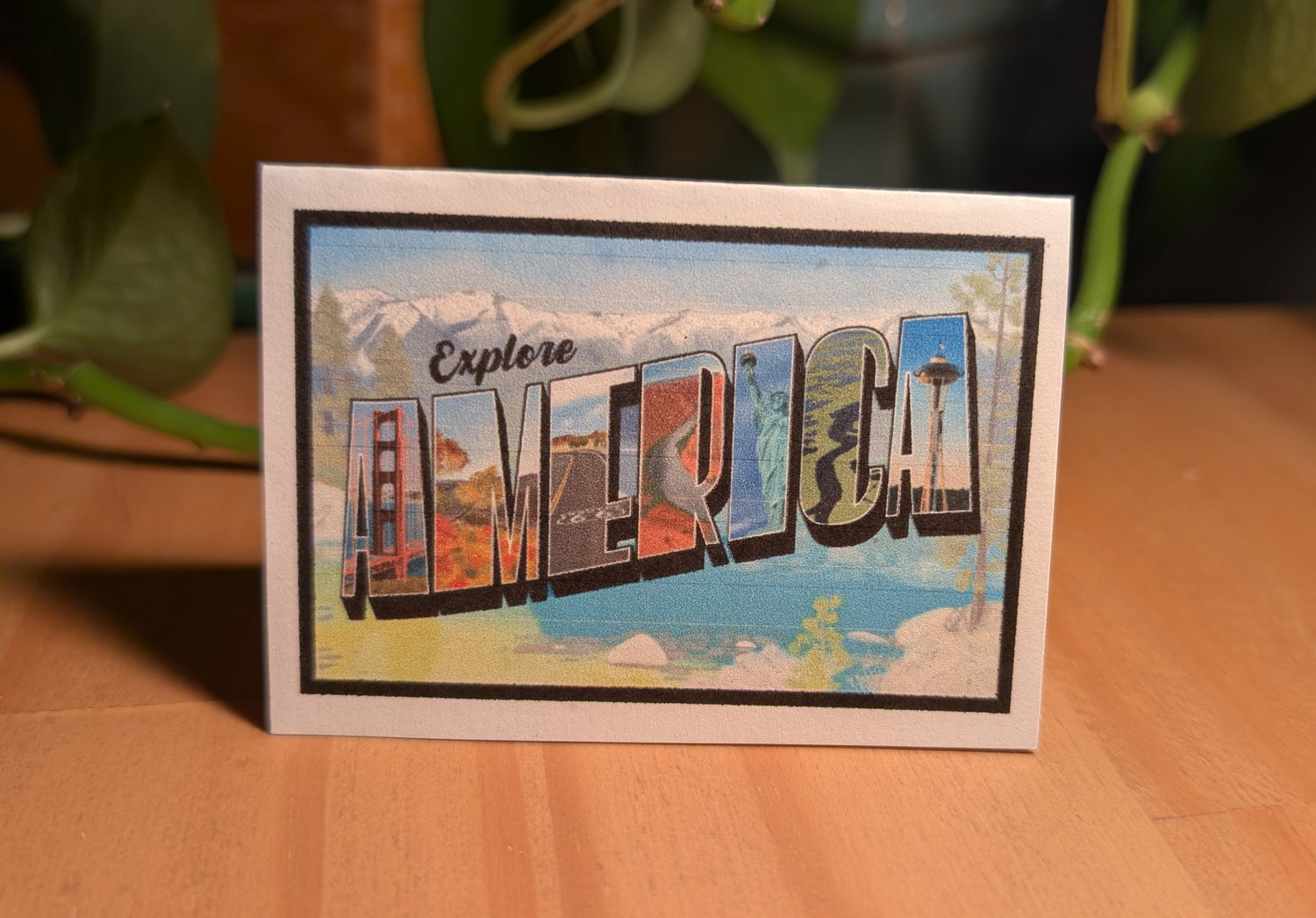 Mini card with America vintage letter art design on confetti white paper standing up on desk with plant in background