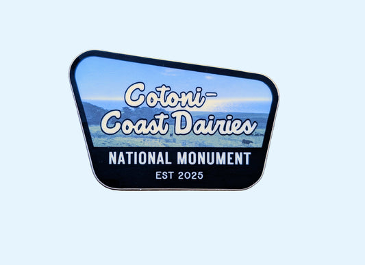 Black-bordered sticker  that reads Cotoni-Coast Dairies National Monument, Est 2025, with a photo of this new local gem north of Santa Cruz, California, USA in the background