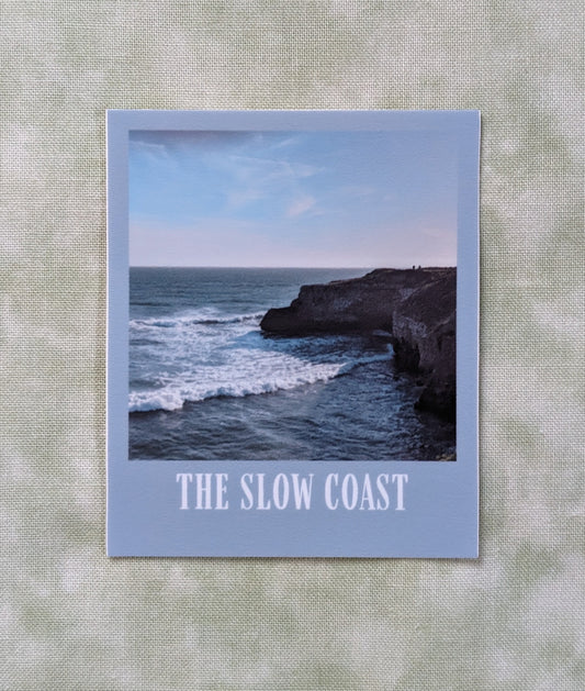 The Slow Coast sticker with a photo of coastal bluffs and a grayish blue border