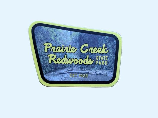 Yellow and brown-bordered sticker reads Prairie Creek Redwoods State Park, Est 1923 with a photo of Fern Canyon in this part of Redwoods National Park, in Northern California, USA in the background