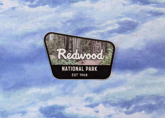 Redwood National Park badge sticker with black border and photo of old growth redwood trail in background