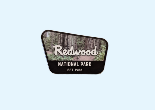 Redwood National Park badge sticker with black border and photo of old growth redwood trail in background