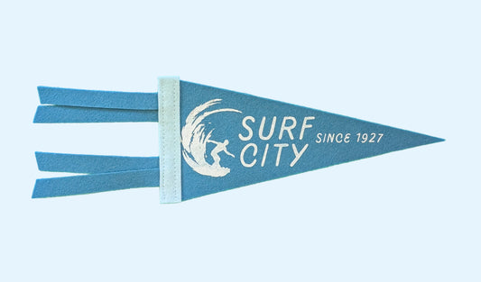 Surf City, Since 1927 souvenir pennant representing Santa Cruz California with a surfer in a wave on blue felt