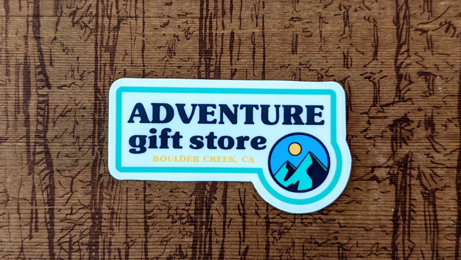 Small sticker reads Adventure Gift Store, Boulder Creek, CA with mini mountain sun circle