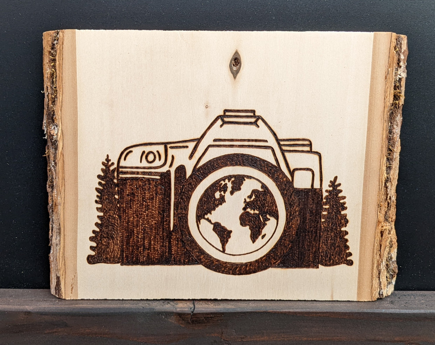 Wood burned Art by Wood Wanderlust - camera with world in view and surrounded by pines