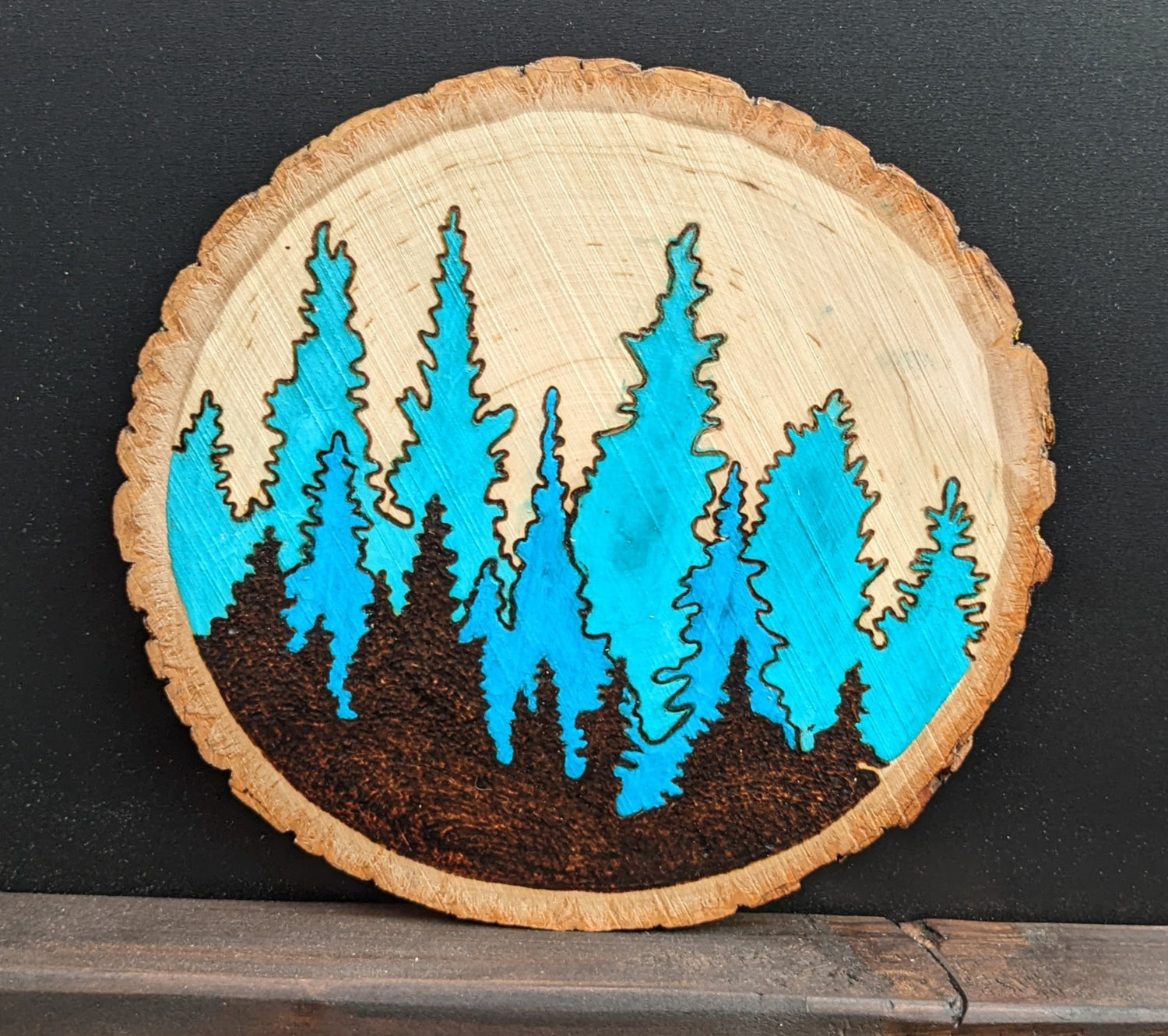 Wood burned Art by Wood Wanderlust of evergreen forest on round log crosscut