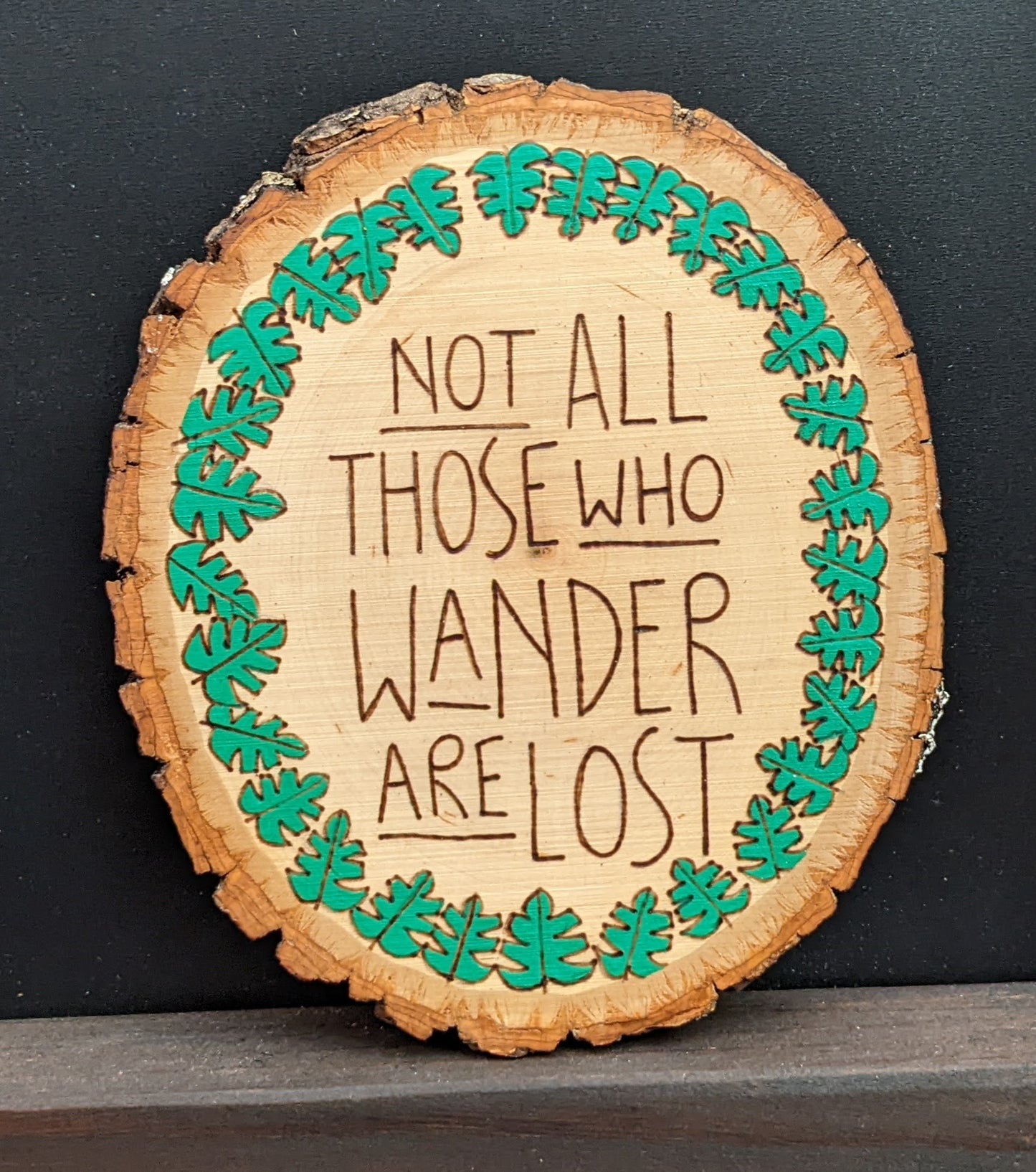 Wood burned Art by Wood Wanderlust round piece with plant border and text art reading Not all those who wander are lost