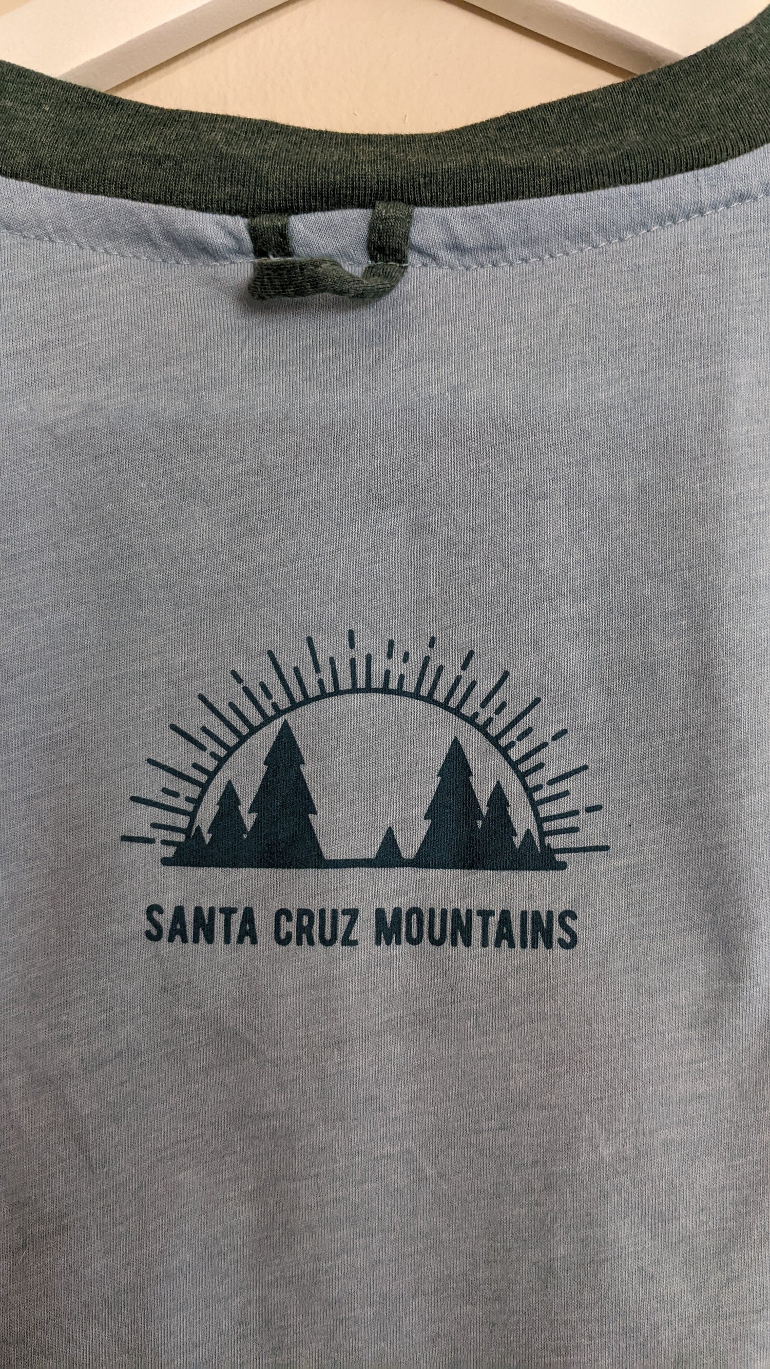 Close up of Santa Cruz Mountains Present logo mark on back of blue and green shirt