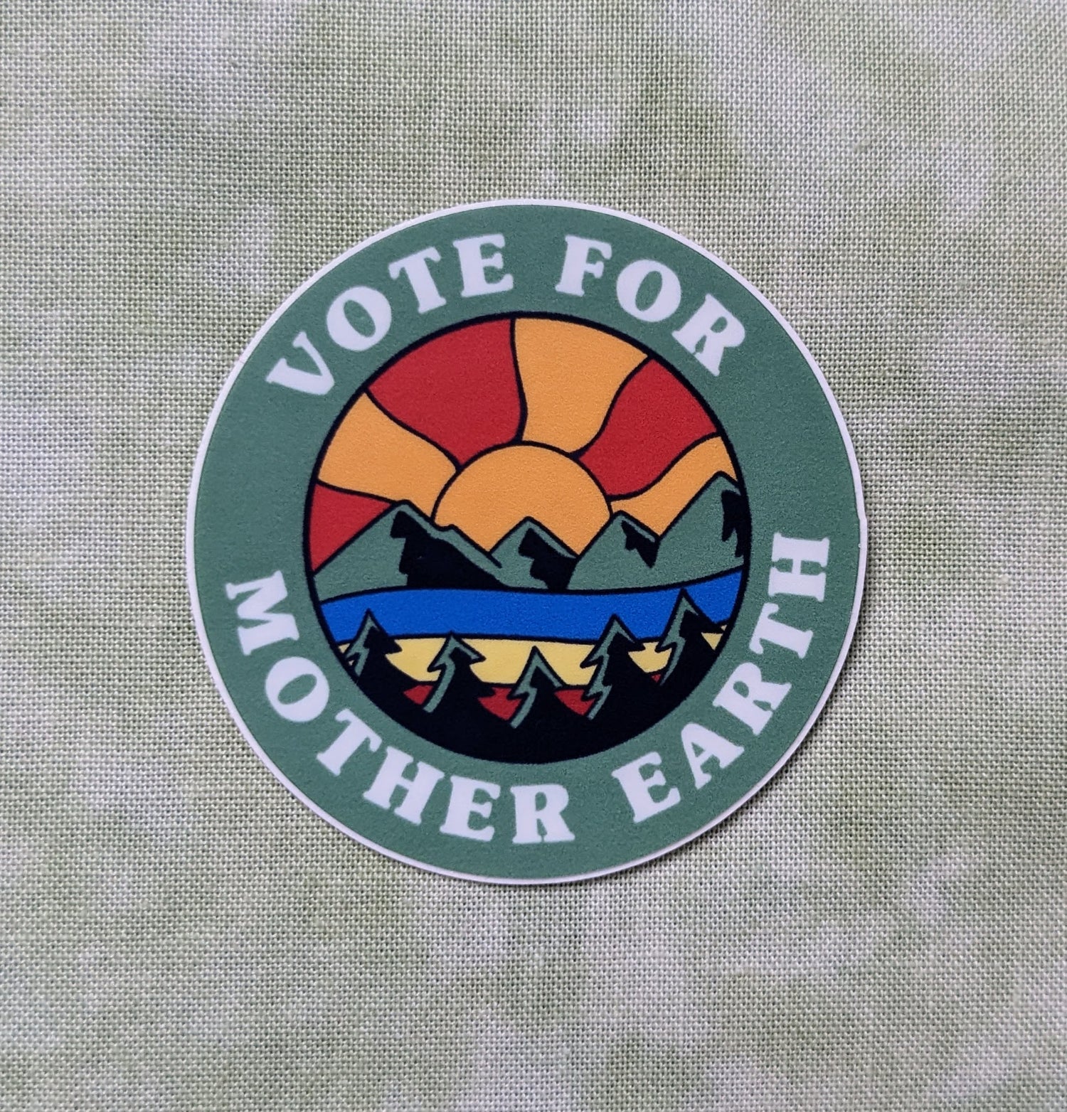 Round sticker that reads Vote for Mother Earth with Mountainscape sunset scene