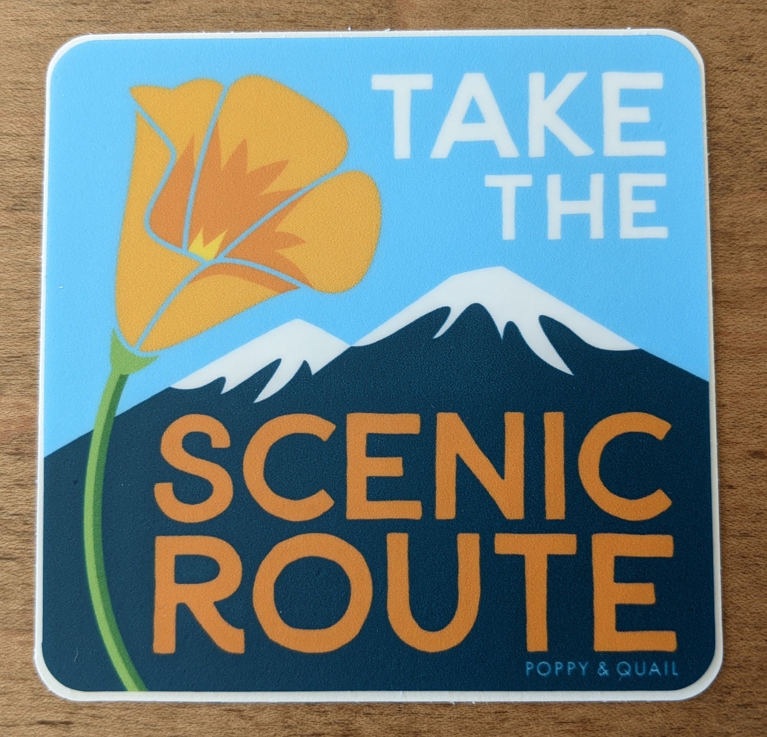 Square sticker with poppy and mountain reading "Take the Scenic Route" by Poppy & Quail
